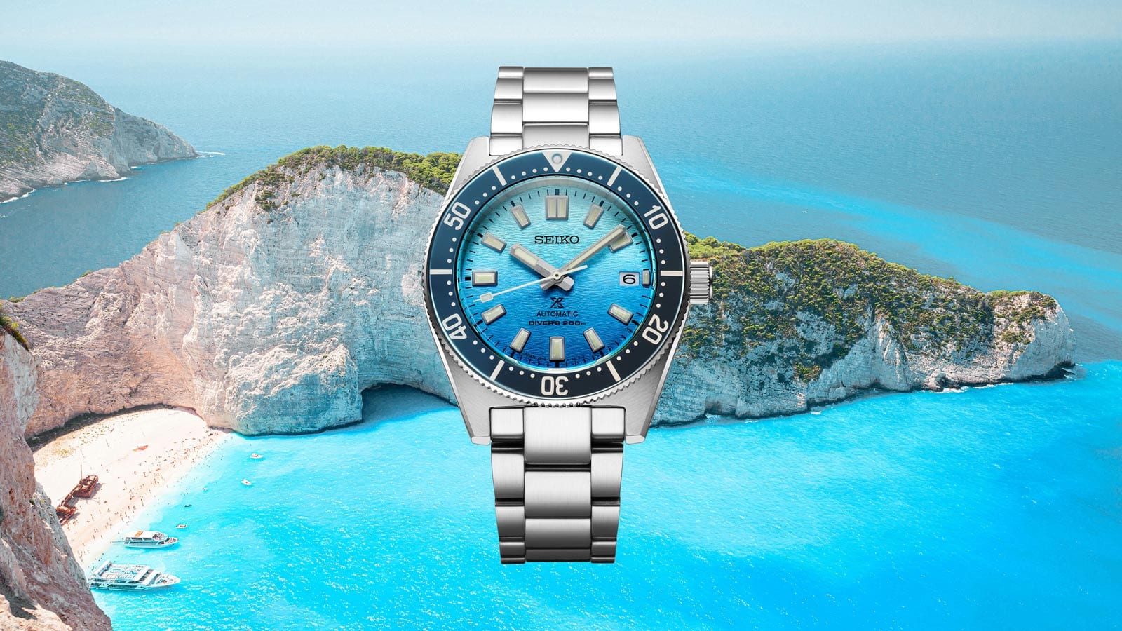 Taucheruhr mit blauem Zifferblatt vor einer beeindruckenden Küstenlandschaft mit klarem Wasser.