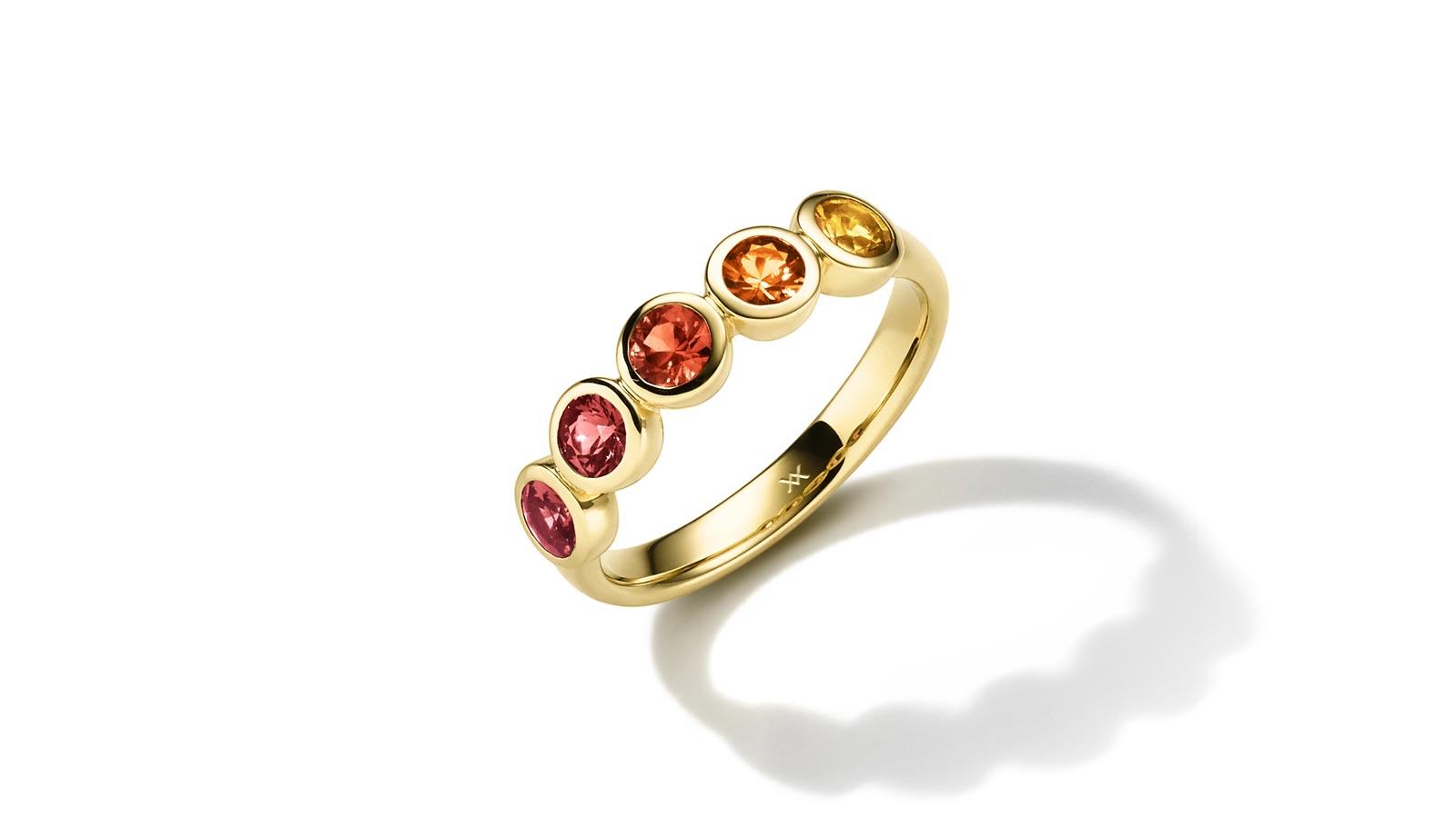 Goldring mit fünf bunten Edelsteinen, die in Rot- und Gelbtönen schimmern, auf weißem Hintergrund.