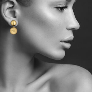 Profil einer Frau mit neutralem Ausdruck, großen goldenen Ohrringen und heller Haut.