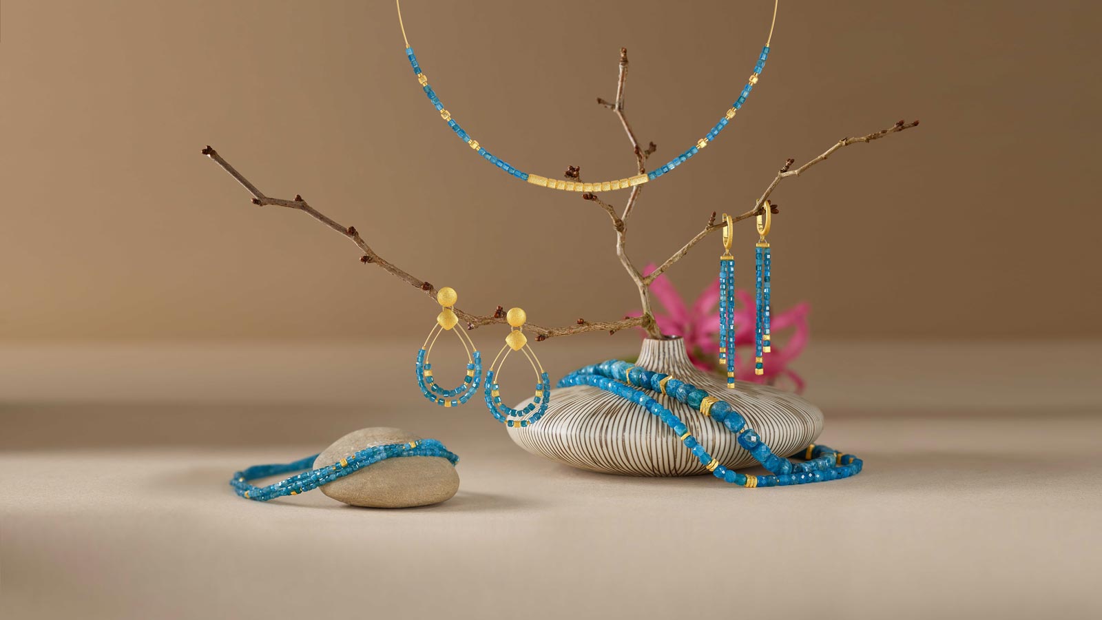 Zweige mit blau-goldenem Schmuck auf beige Hintergrund, pinke Blumen im Hintergrund