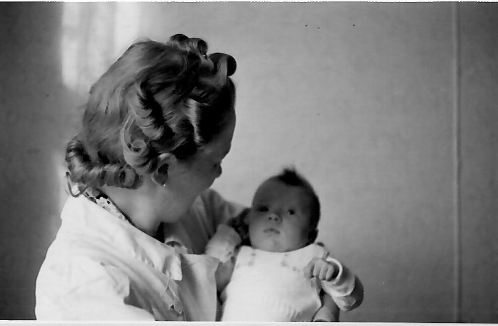 Eine Frau mit lockigem Haar hält ein Baby im Arm, beide schauen ruhig drein