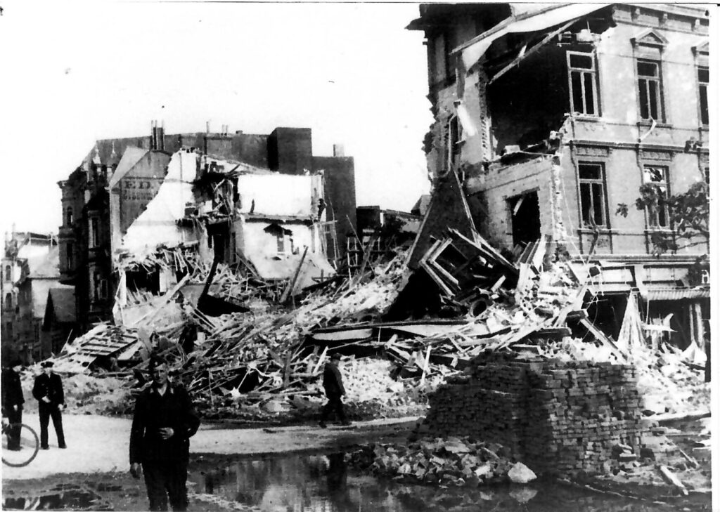 Ein Mann steht ernst vor zerstörten Gebäuden und Trümmern in einer schwarzweißen Szene