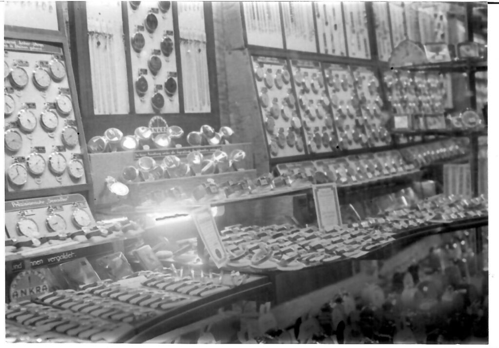 Ein Schwarzweißbild zeigt zahlreiche Uhren und Schmuck in einer Vitrine eines Ladens