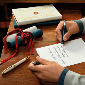 Eine Person mit hellem Sakko schreibt mit einem blauen Stift auf weißem Papier