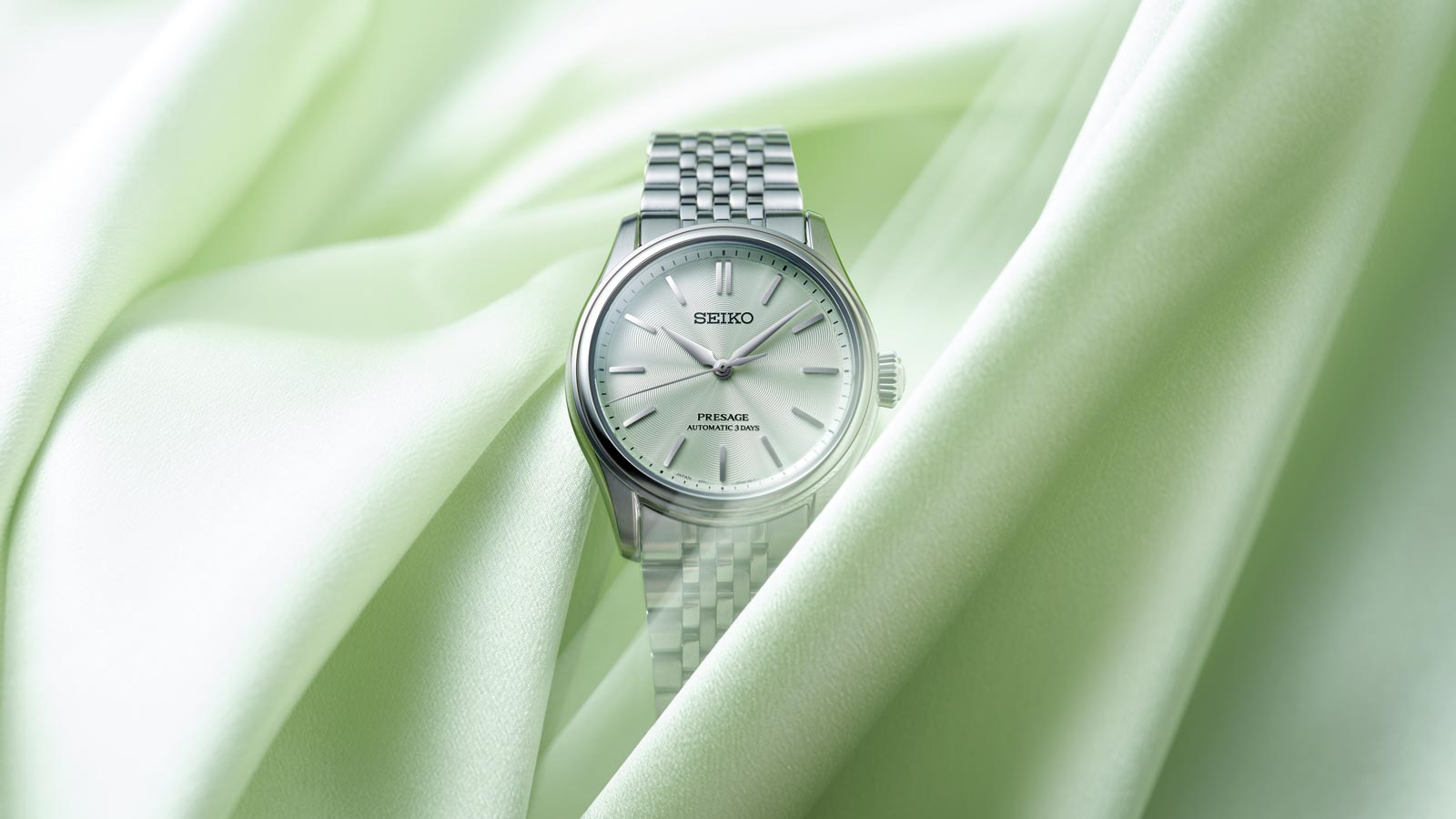 Silberne Seiko Presage Automatikuhr auf hellgruenem Seidenstoff