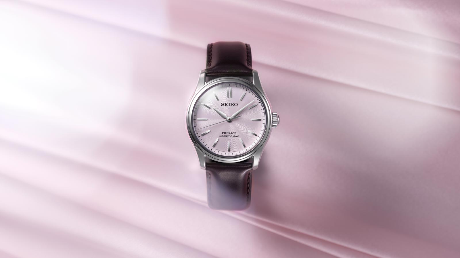 Eine Seiko Presage Automatikuhr mit hellem Zifferblatt auf rosa Seidenstoff